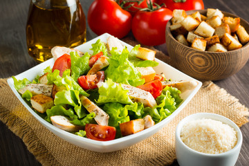 Fresh salad with delicious chicken breast, ruccola, spinach, cabbage, arugula and tomato on wooden background. Oil, salt and pepper.