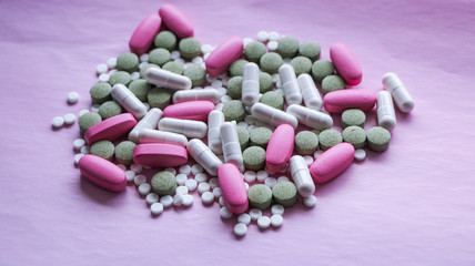 white, pink and green pills on a pink background. multi-colored drugs.