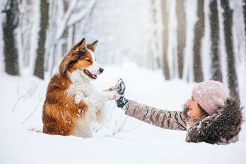 Beautiful young woman and funny red dog are walking in the snow in the park. They walk and play in the snowstorm.
