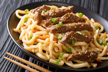 Fried beef with teriyaki sauce and sesame served with udon, carrot and green onions close-up on a...