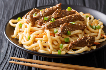 Asian spicy teriyaki beef served with udon, carrot and green onions closeup on a plate. horizontal
