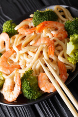 Japanese healthy food: udon noodles with shrimps and broccoli closeup on a plate. vertical