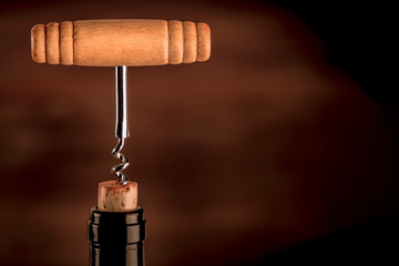 A side view closeup of a vintage corkscrew in a bottle of wine, on a dark background with a place for text, sepia toned image