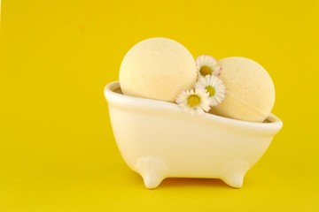 bath Bomb with chamomile extract. yellow  bath bombs with chamomile flowers in a decorative ceramic bath on a bright yellow background.Organic body cosmetics  with chamomile essential oil.