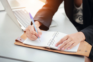 businesswoman writing on notebook with laptop computer