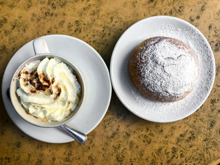 Coffee with whipped cream and homemade bun with icing sugar