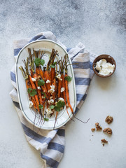 Baked young orange carrots with soft cheese, walnuts and cilantro on white oval plate. Top view.