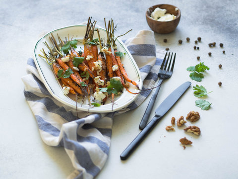 Baked young orange carrots with soft cheese, walnuts and cilantro on white oval plate.
