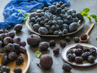 Purple fruits and berries. Blackberries, grapes, plums and figs in a wooden tray and metal plates on dark background. Tasty and ripe fruits and berries.