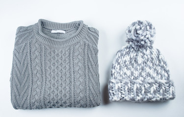 Collection of woolen winter clothes - knitted sweater and hat on white background table. Top view, flat lay