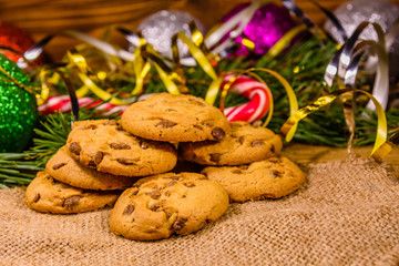 Pile of the chocolate chip cookies on sackcloth in front of christmas decorations