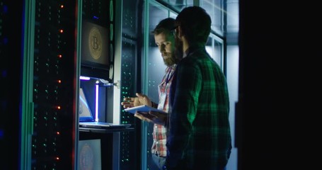 Adult men coworking in corridor of server room with racks around and setting hardware of bitcoin mining farm - Powered by Adobe