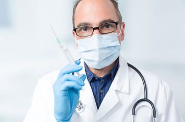 Hausarzt mit Mundschutz hält eine aufgezogene Spritze in der Hand