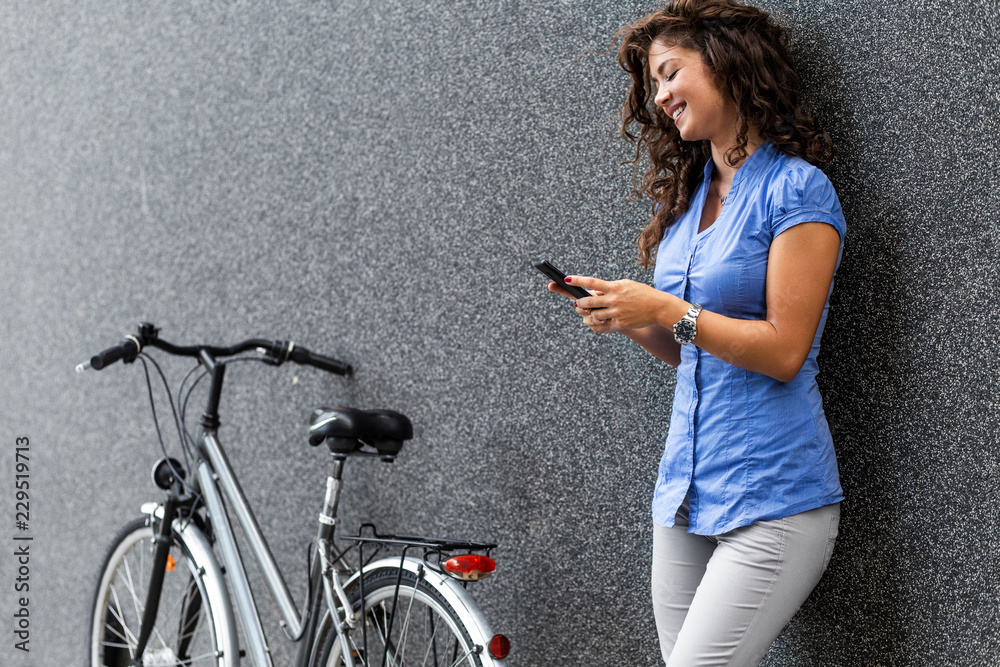 Wall mural portrait of businesswoman with her bicycle looking at mobile phone.