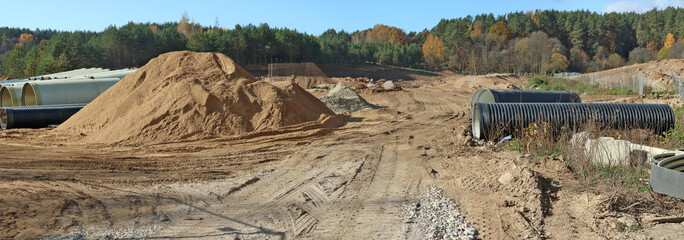 Large sewer pipes and heaps of sand with traces of heavy equipment wheels on a construction site in...