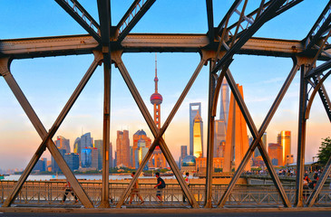 people walking on historical Waibaidu iron bridge in front of the futuristic modern skyline of Pudong Shanghai, China