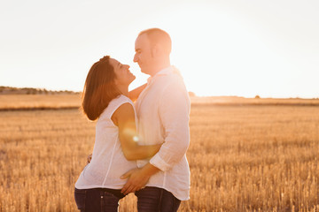 portrait outdoors of a young young pregnant couple in a yellow field. Outdoors family lifestyle.