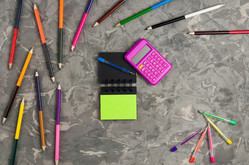 Blank paper notebook and blue pen and pink calculator near stationery supplies on gray scratched concrete table. Top view. Business or education concept