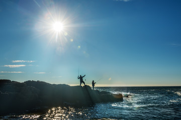 Silhouettes of fishermen on the rocks catch fish on the shores of the Atlantic Ocean. USA. Maine....