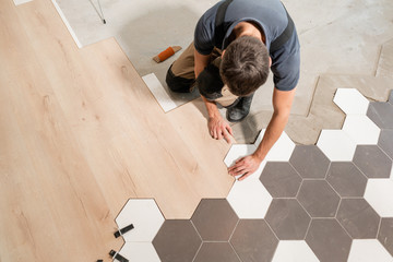 Male worker installing new wooden laminate flooring. The combination of wood panels of laminate and ceramic tiles in the form of honeycomb. Kitchen renovation. - 229521757