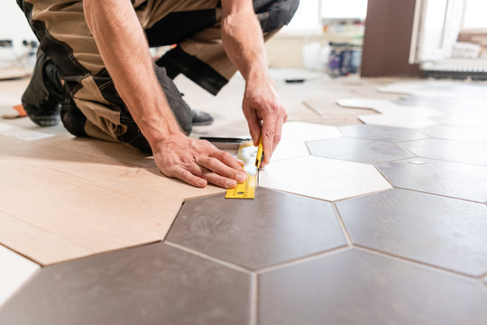 Male worker makes measurements and installing new wooden laminate flooring. The combination of wood panels of laminate and ceramic tiles in the form of honeycomb. Kitchen renovation.
