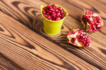 Fototapeta na wymiar Two halves of fresh ripe red pomegranate with seeds near full green metal bucket of seeds on old brown weathered rustic wooden table