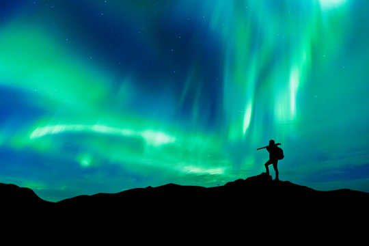 Aurora borealis with silhouette standing photographer on the mountain.Freedom traveller journey concept