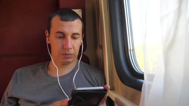 man listening to the music on the train rail car coupe compartment travel. slow motion video. man with a lifestyle smartphone at the window of a train in a car travel internet social media web. man