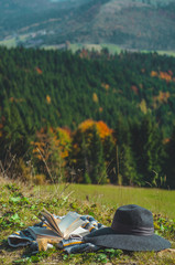 Fototapeta premium Carpathian alpine mountain. Pages of an open book, hat and thermo cup. Majestic landscape. Nature and education concept.