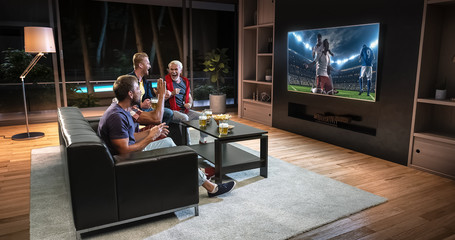 Group of fans are watching a soccer moment on the TV and celebrating a goal, sitting on the couch...