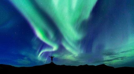 Aurora borealis with silhouette standing man on the mountain.Freedom traveller journey concept