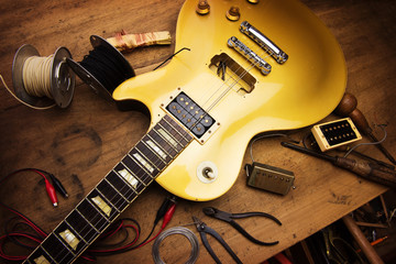 Electric guitar repair. Vintage electric guitar on a guitar repair work shop. Single cutaway solid body guitar, gold color. shallow depth of view, intentionally shot with low key shadows. - obrazy, fototapety, plakaty