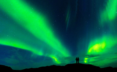 Obraz na płótnie Canvas Aurora borealis with silhouette love romantic couple on the mountain.Honeymoon travel concept