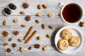 Tasty cookies with black tea, nuts, almonds, anise stars, brown sugar, dates and cinnamon sticks on wooden background, top view, Christmas concept.