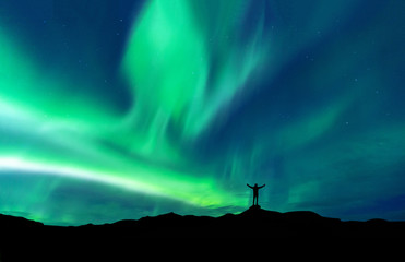 Aurora borealis with silhouette standing man on the mountain.Freedom traveller journey concept