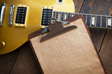 Vintage clipboard with gold electric guitar in background. Good for playlists, and production notes.