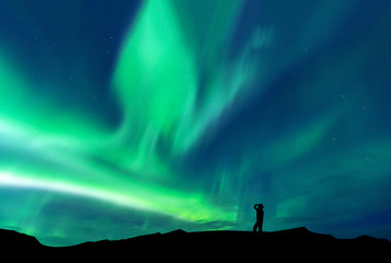 Obraz na płótnie Canvas Aurora borealis with silhouette standing man on the mountain.Freedom traveller journey concept