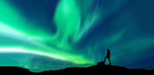 Aurora borealis with silhouette standing man on the mountain.Freedom traveller journey concept