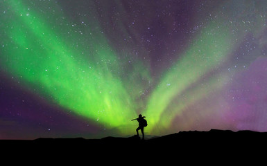 Naklejka na ściany i meble Aurora borealis with silhouette standing photographer on the mountain.Freedom traveller journey concept