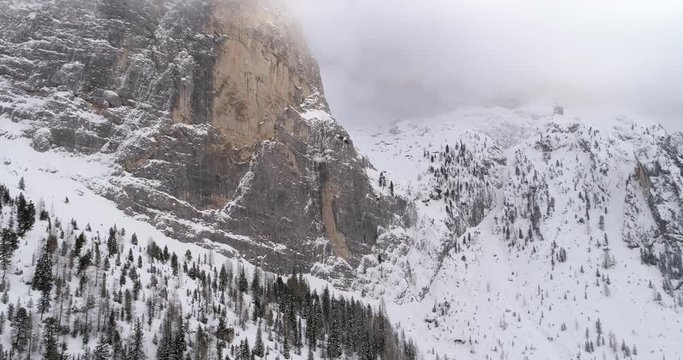 Backward aerial with snowy mountain and woods forest at Sella pass.Cloudy bad overcast foggy weather.Winter Dolomites Italian Alps mountains outdoor nature establisher.4k drone flight