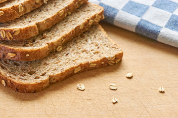 Close-up of slices of whole grain bread on a wooden cutting board with bran and a blue and white checkered cloth in the background