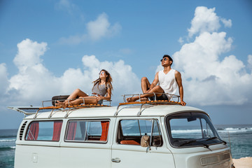 young couple with sunglasses sitting on top of minivan roof