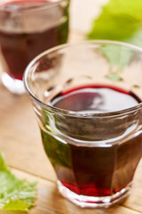 Two informal wine glasses without foot on a table filled with red wine and a green grape leafs. Vertical dutch angle shot with selective focus