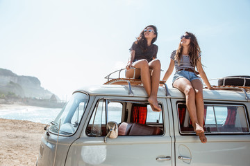 young women with sunglasses sitting on top of minivan roof