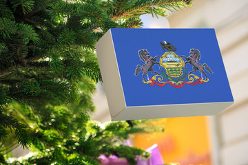 Pennsylvania state flag printed on a Christmas gift box. Printed present box decorations on a Xmas tree branch on a street. Christmas shopping in United States, local market sale and deals concept.