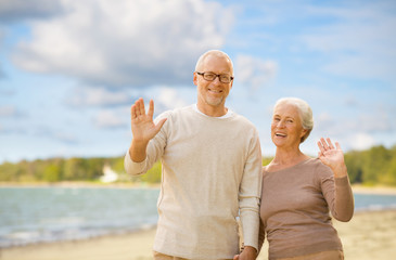 old age, retirement and people concept - happy senior couple waving hands over beach background