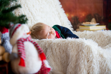 Obraz premium Baby boy, cute child, wearing santa claus robe sitting in rocking chair with Christmas tree and lights on