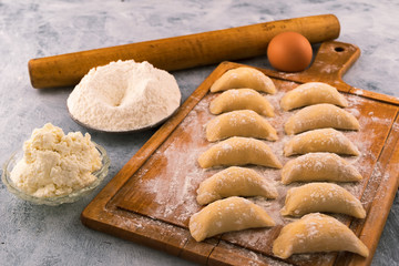 Homemade dumplings stuffed with cottage cheese, stacked in rows on a wooden chopping Board.