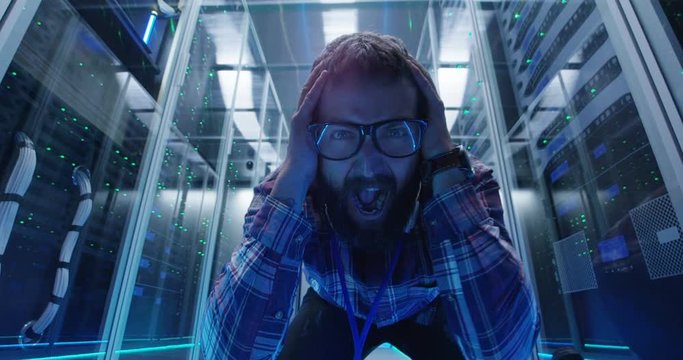 Adult bearded man in glasses and checkered shirt showing various grimaces at camera in server room of data center