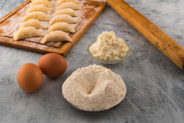 Sifted flour on a round plate, cottage cheese for filling, chicken eggs for dough-ingredients for cooking homemade dumplings.